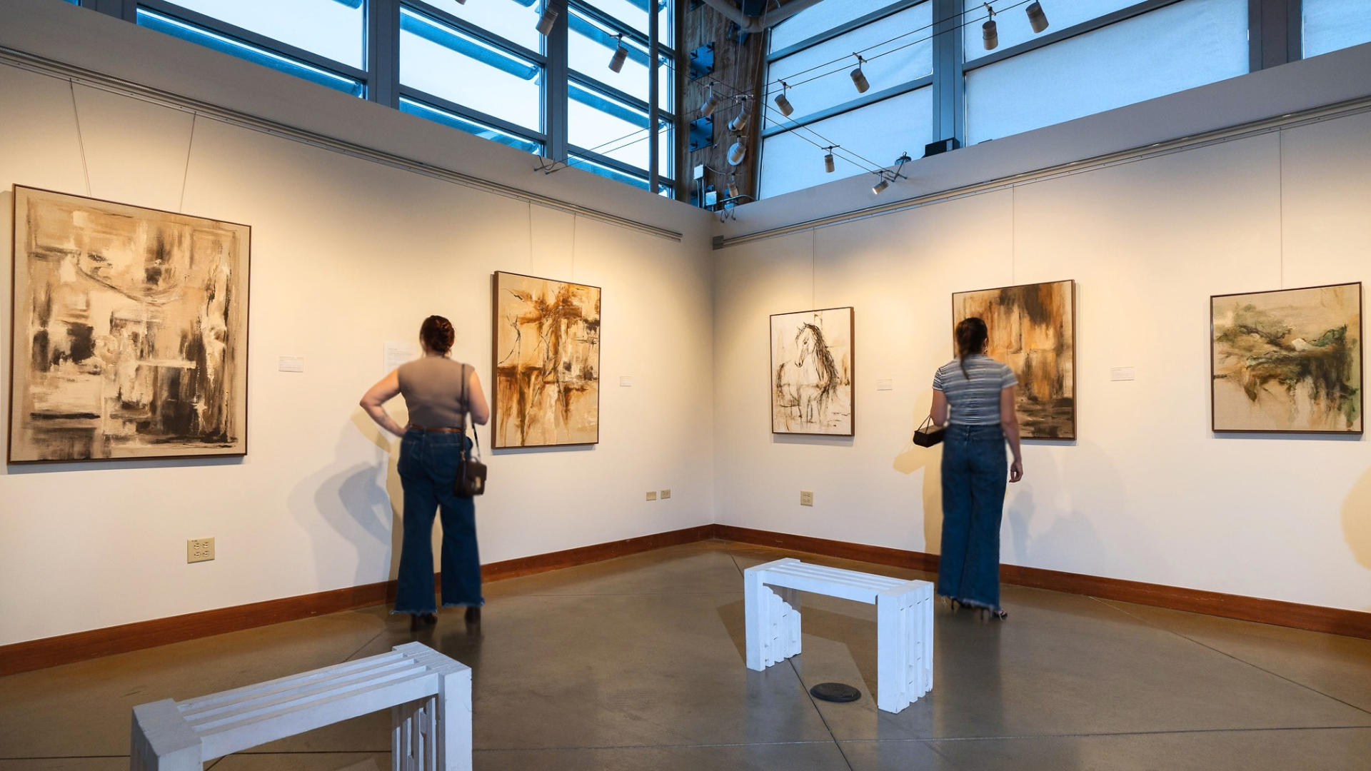 Two visitors viewing paintings, including White Horse, at the Becoming Home exhibition.